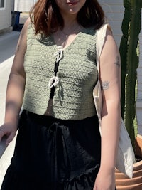a woman wearing a green crocheted vest and black skirt