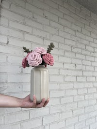a hand holding a crocheted vase of pink flowers
