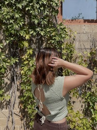 a woman is standing in front of a wall with ivy growing on it