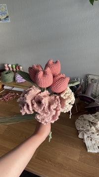 a hand holding a crocheted bouquet of pink flowers