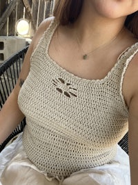 a woman sitting on a chair wearing a crocheted top